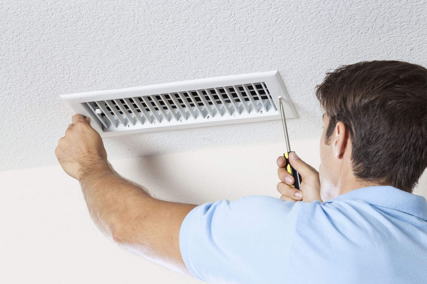 A man is working on a vent in a room, highlighting HVAC mold removal services in Orlando, FL.