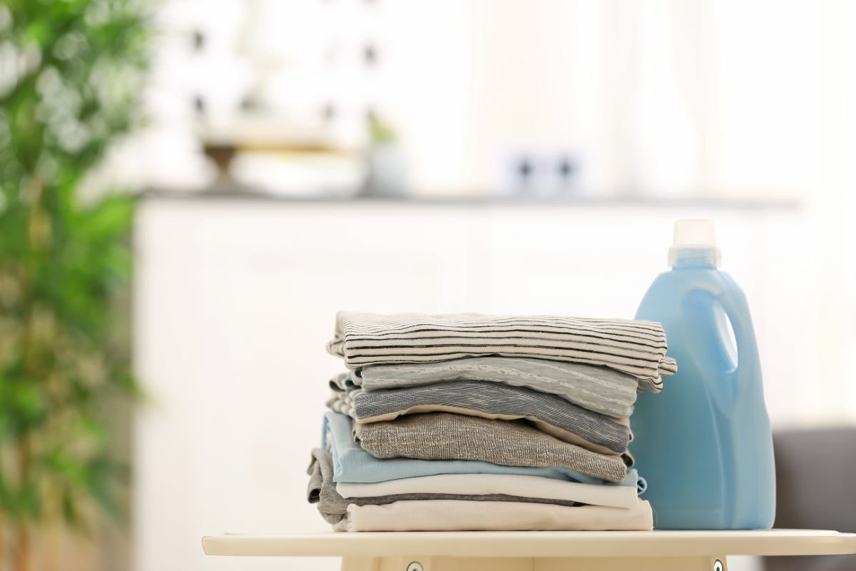 A neatly arranged stack of laundry on a table accompanied by a bottle of detergent, illustrating household chores.